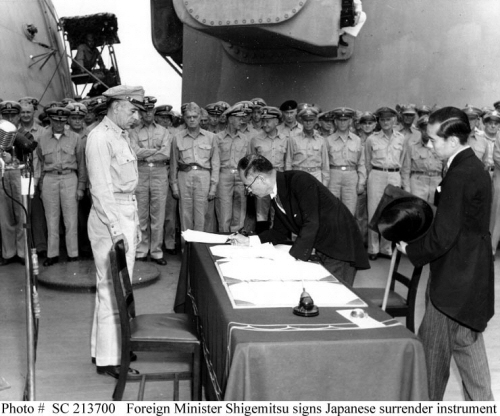 Japanese Foreign Minister Mamoru Shigemitsu signs the Instrument of Surrender on behalf of the Japanese Government, on board USS Missouri (BB-63), 2 September 1945. Lieutentant General Richard K. Sutherland, U.S. Army, watches from the opposite side of the table. Foreign Ministry representative Toshikazu Kase is assisting Mr. Shigemitsu.  Photograph from the Army Signal Corps Collection in the U.S. National Archives.